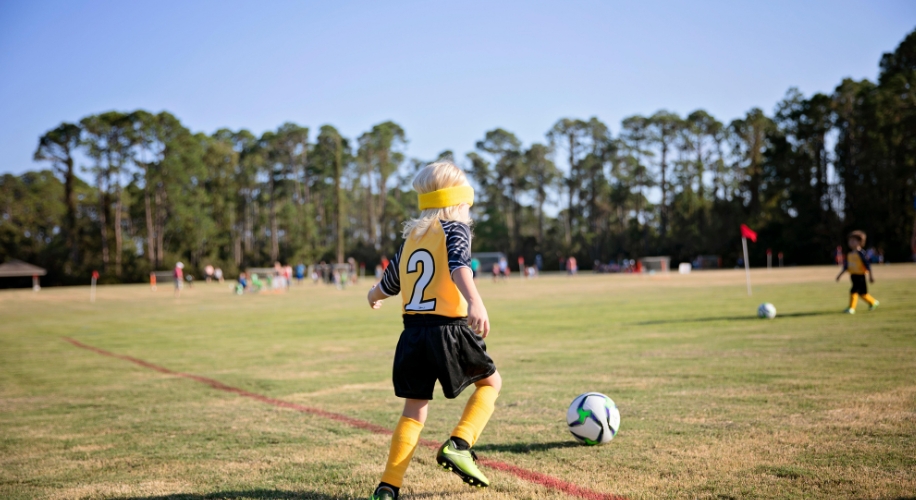 Child in yellow soccer uniform with the number 2 playing on an open grassy field.