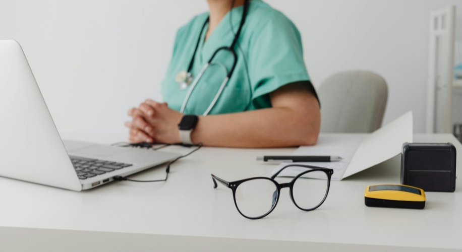 Glasses, yellow glucose meter, laptop, and documents on a medical professional&#039;s desk.