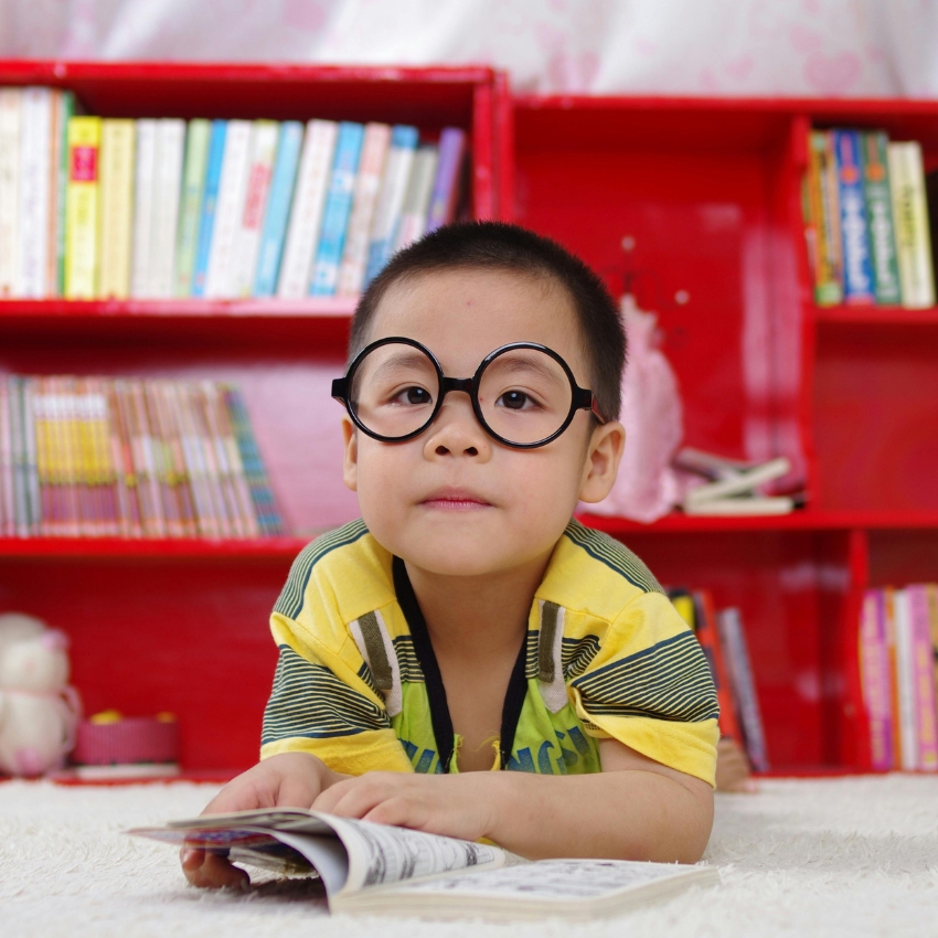 Child wearing round glasses and a yellow striped shirt reading a book.