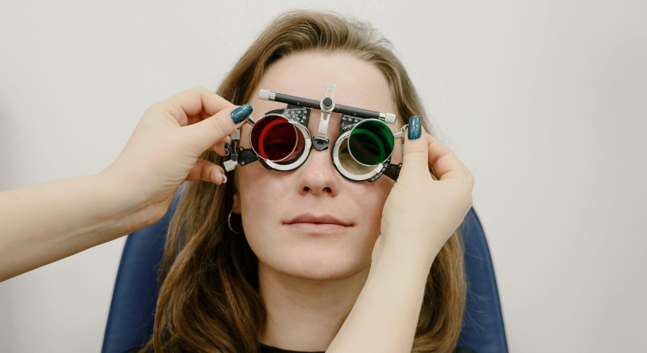 Woman wearing trial frame with red and green lenses during eye exam.