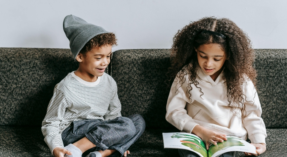 Two children sitting on a couch reading a colorful book together.