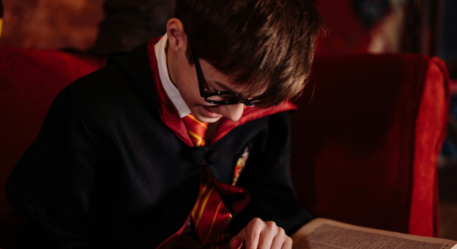 A person wearing glasses and a robe with a red and yellow tie, looking at an open book.