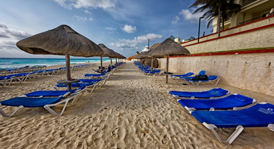 Blue lounge chairs with thatched umbrellas lined up on a sandy beach.