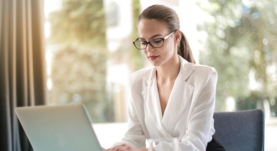 Professional woman wearing glasses and a white blazer, working on a laptop.