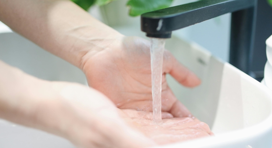 Hands being washed under a running black faucet in a white sink.