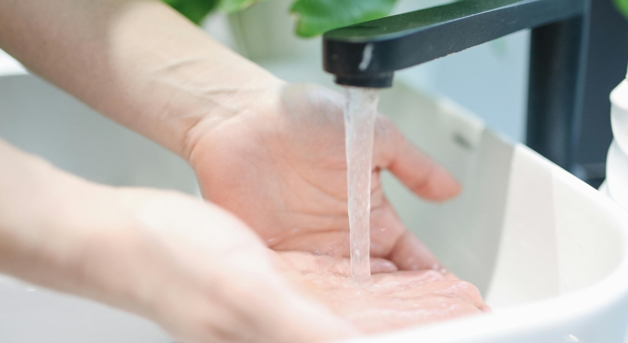 Hands under running water from a black faucet in a white sink.