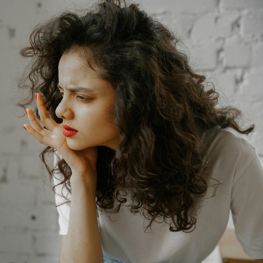 Woman with curly hair, red lipstick, and white shirt looking sideways contemplatively.