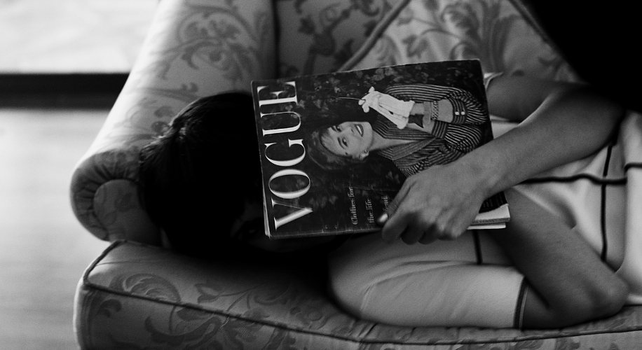 Person holding Vogue magazine while lying on a patterned couch. Cover features a woman in striped attire.