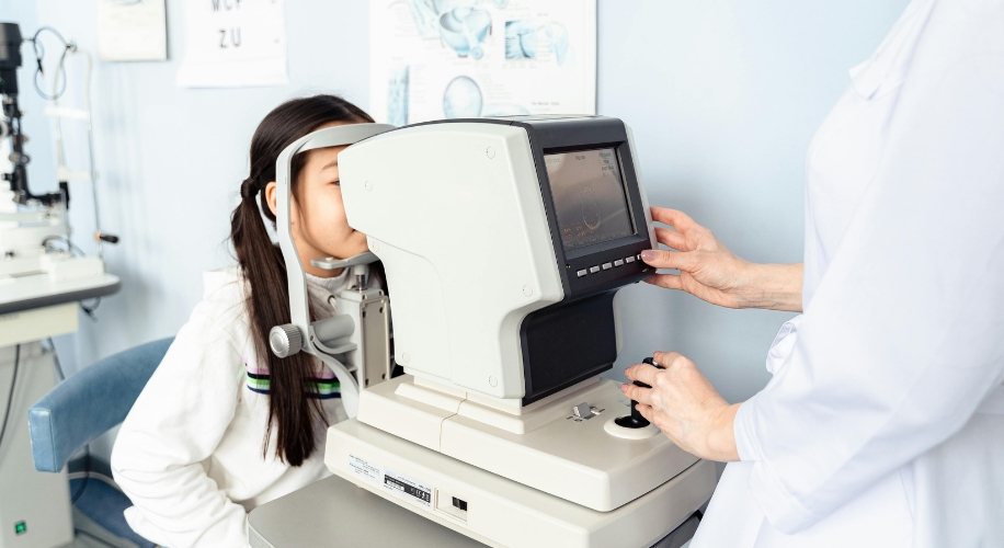 Child undergoing an eye examination using an autorefractor operated by a healthcare professional.