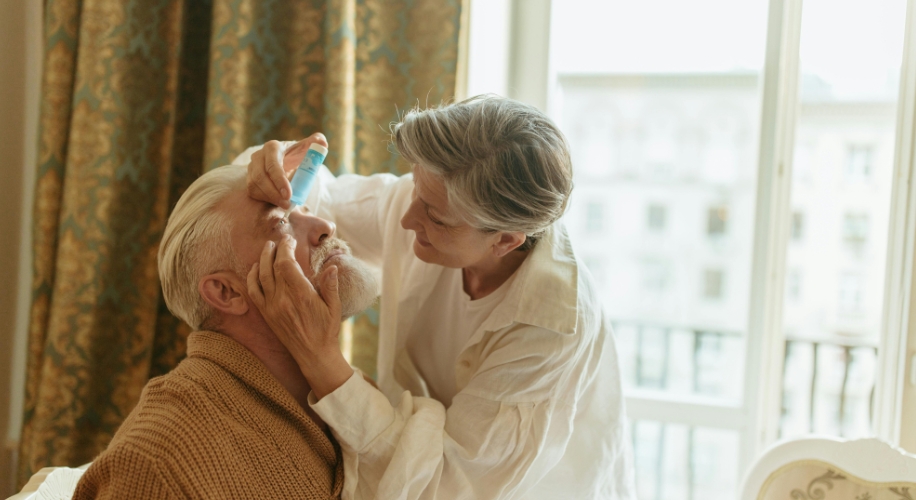 Person administering eye drops to an elderly man&#039;s eye.