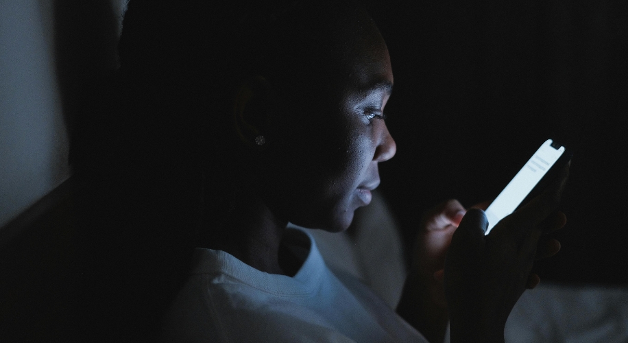 Person using a smartphone in a dark room, screen illuminates the user&#039;s face.