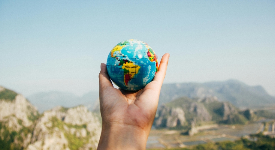 Hand holding a small globe showing continents and countries including North America and Africa.