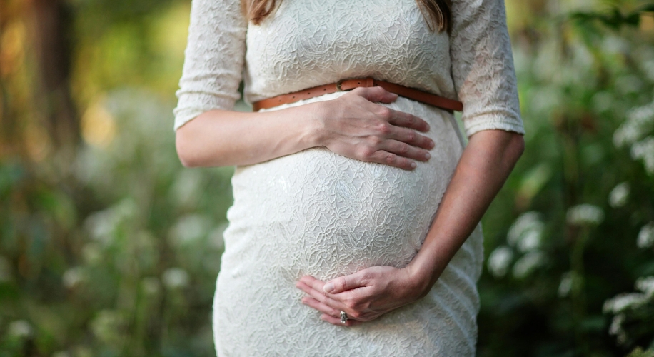 Pregnant woman in a lace dress with hands on her belly.