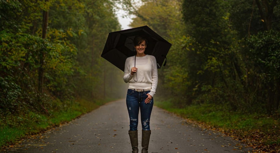 Person holding a black umbrella while wearing a cream sweater, blue jeans, and brown boots.