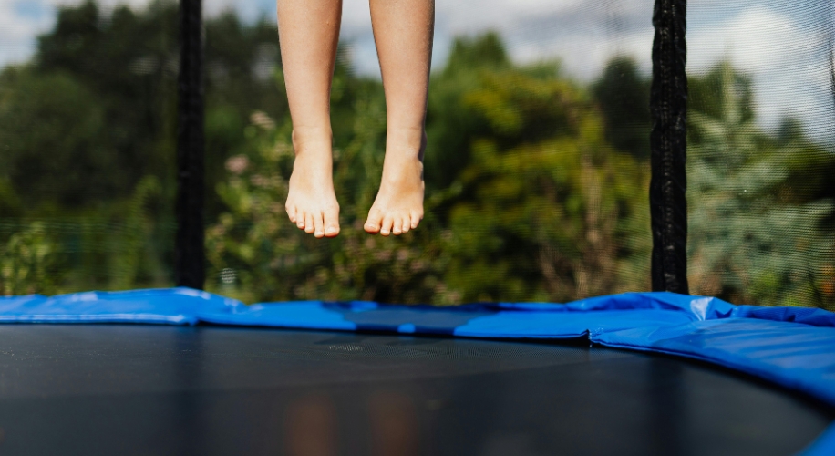 Feet mid-air while jumping on a trampoline with blue safety padding.