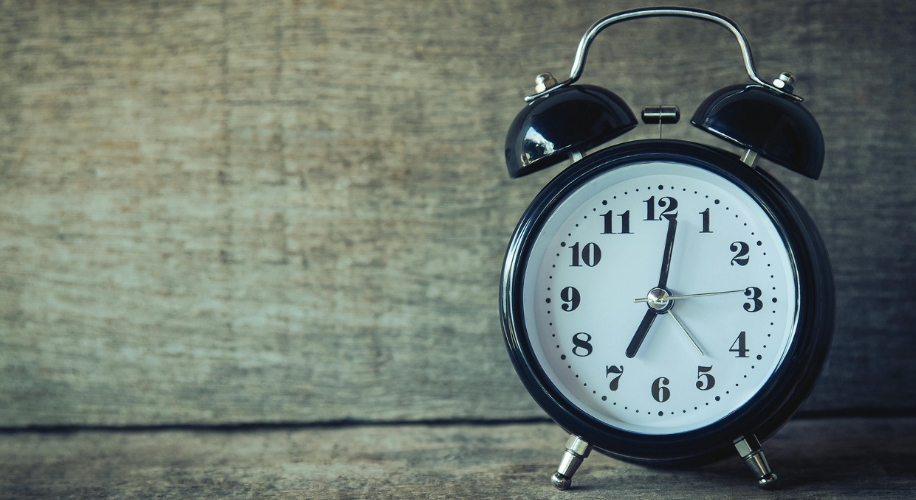 Black retro alarm clock with white face, two bells on top, showing 10:09.