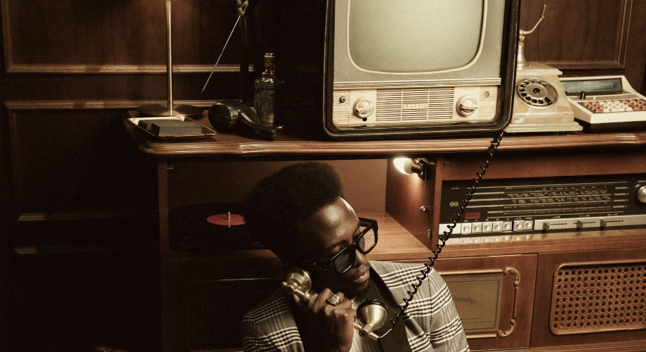 Retro TV, rotary phone, and man on corded phone with record player in vintage setting.