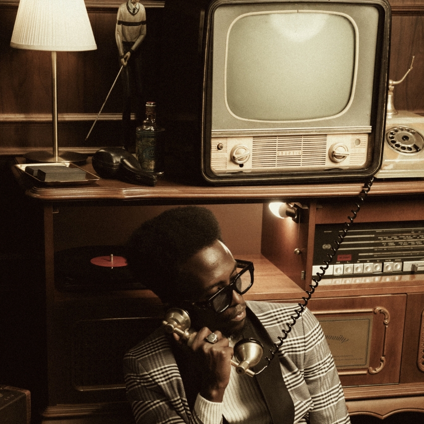 Vintage television with dials and knobs sits on a shelf above a person using a rotary phone.