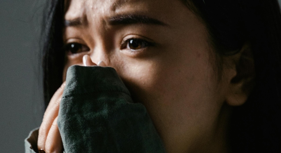 Close-up of a person in distress, covering their mouth with their hand and looking upward.