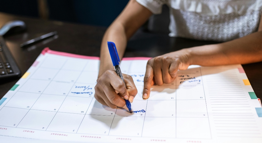 Hands writing on a calendar with a blue pen.