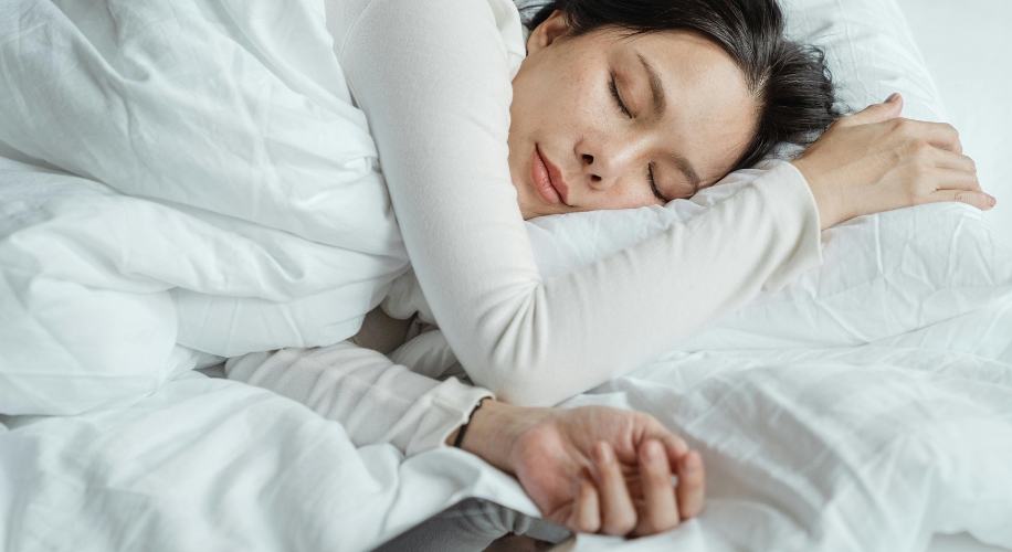 A person sleeping peacefully on a white bed, wearing a white long-sleeve shirt.