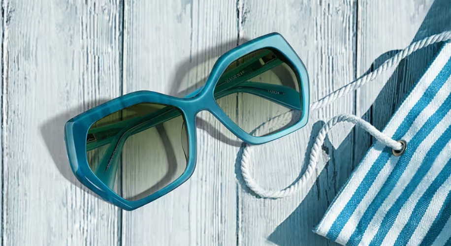 Retro teal hexagonal sunglasses with dark green lenses next to a striped teal and white cloth.