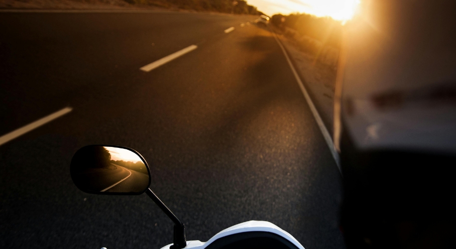 Motorbike handlebar and mirror reflecting a curved road at sunset.