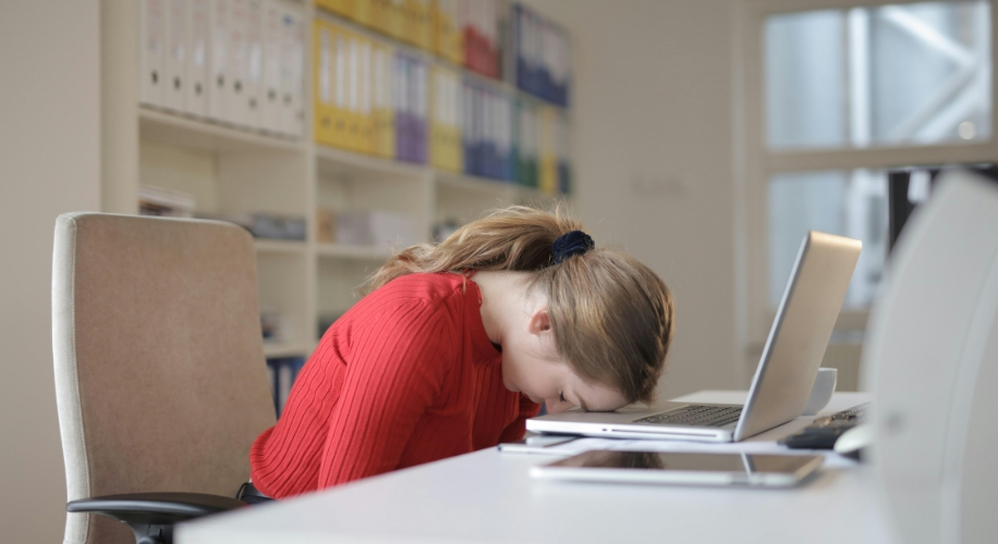 Person resting head on open laptop next to a tablet.