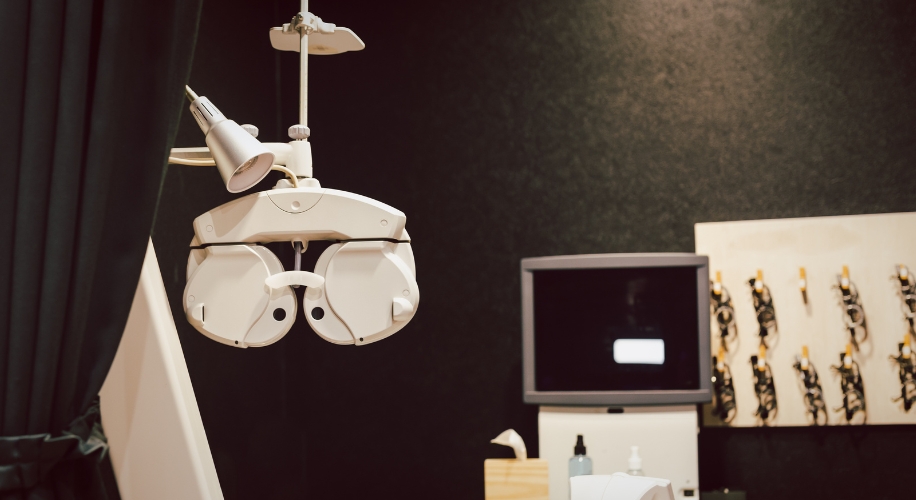 Optometry phoropter machine with overhead lamp in an eye examination room.