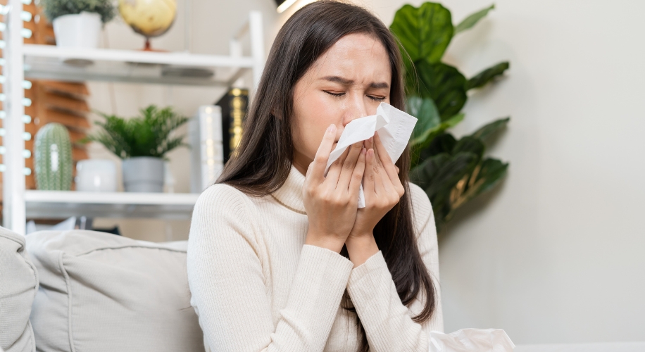 Woman blowing her nose with a tissue, appearing to have allergies or a cold.