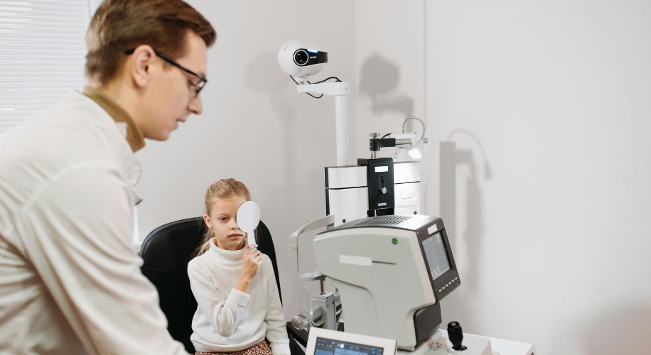 Optometrist examining a child&#039;s vision using an autorefractor machine in an eye clinic.