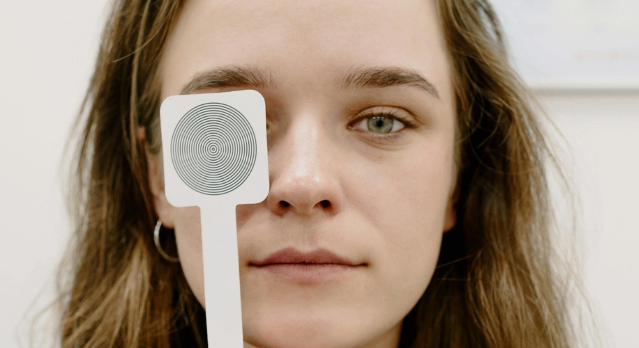 Woman holding an eye exam occluder with a concentric circle design over her left eye.