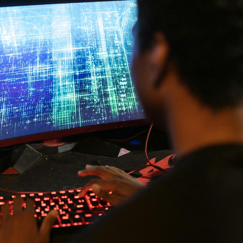 Person typing on a backlit red keyboard with abstract digital rain pattern on a wide computer monitor.