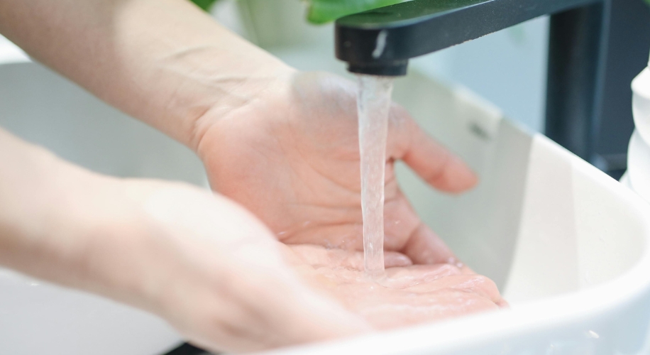 Hands being washed under running water from a faucet.