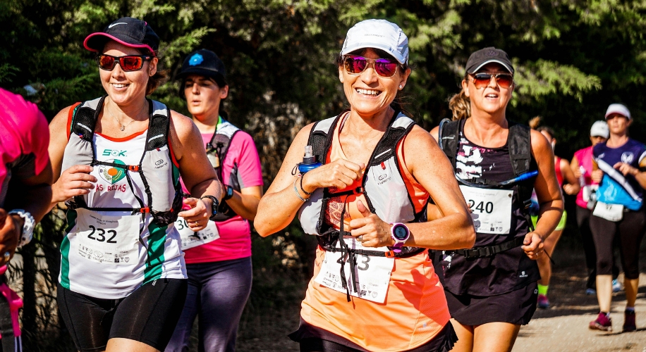 Group of runners wearing race numbers, hydration vests, and sunglasses, smiling during a marathon.