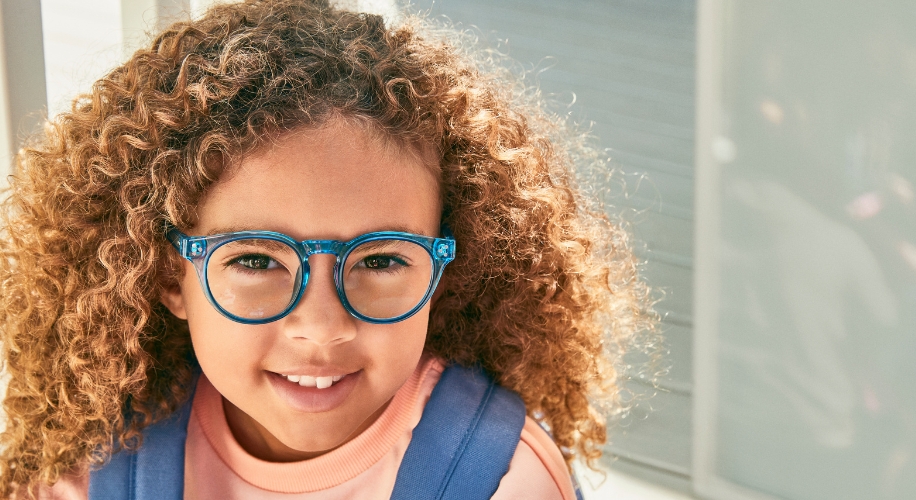 Child wearing blue eyeglasses with thick rims and a pink sweater.