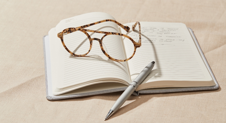 Tortoiseshell glasses and a silver pen on an open lined notebook with handwritten text.