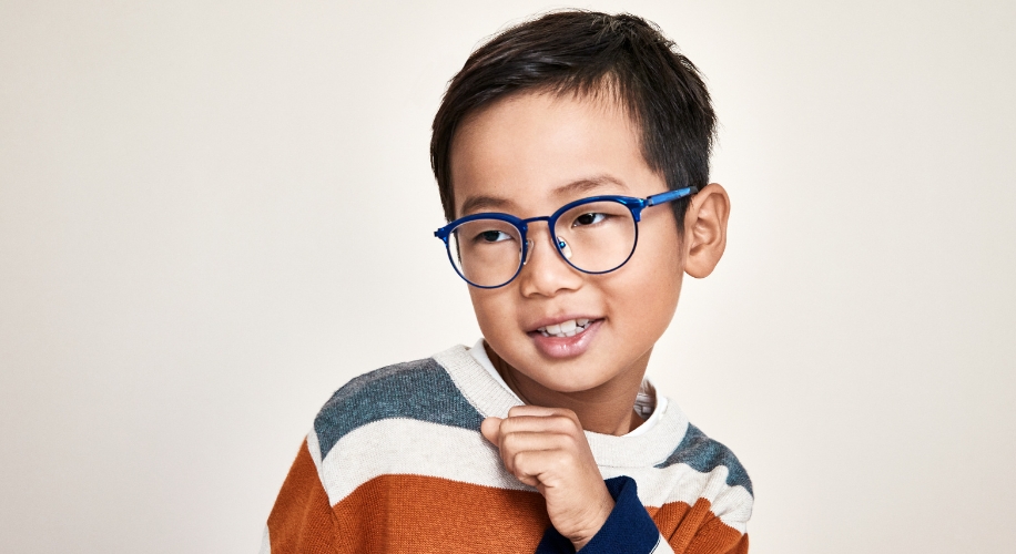 Child wearing blue eyeglasses and a striped sweater with shades of gray, white, and orange.