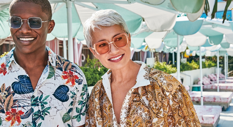 Two people wearing patterned shirts and sunglasses, smiling.