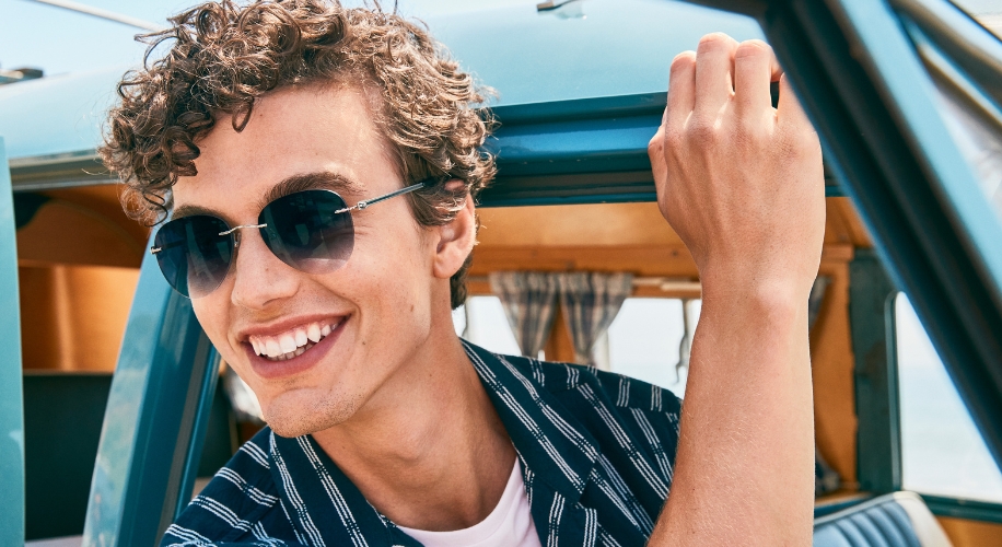 Smiling man wearing round sunglasses and a blue pinstripe shirt.