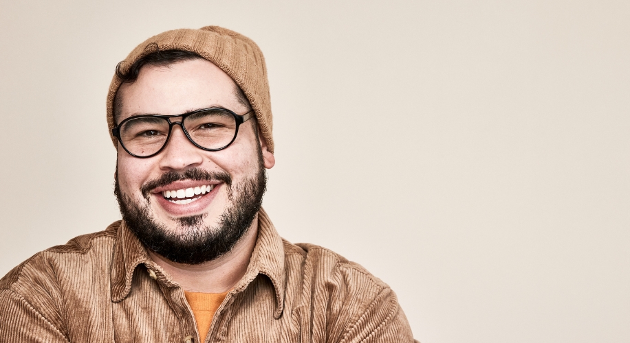 Smiling man wearing black-rimmed glasses, a brown beanie, and a brown corduroy shirt.