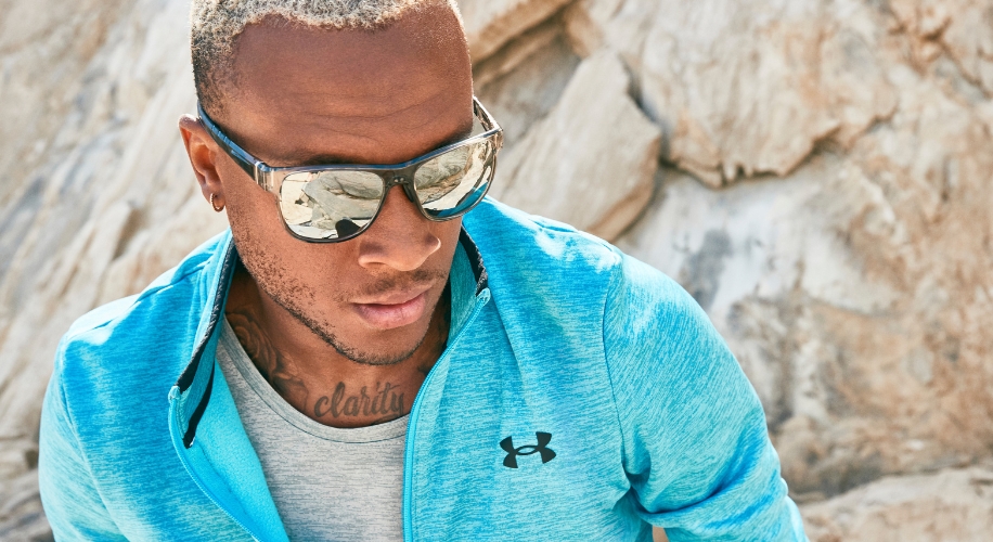 Man wearing mirrored sports sunglasses and a blue Under Armour zip-up jacket, &quot;clarity&quot; tattoo on chest.