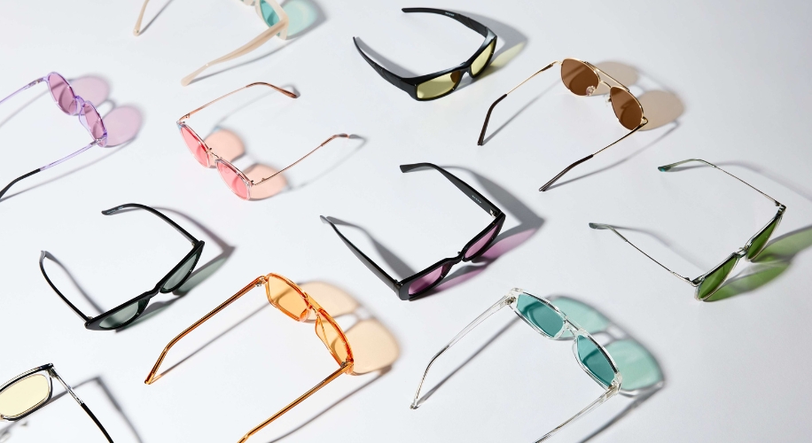 Assorted sunglasses in various shapes and colors, including black, pink, orange, green, and transparent frames.