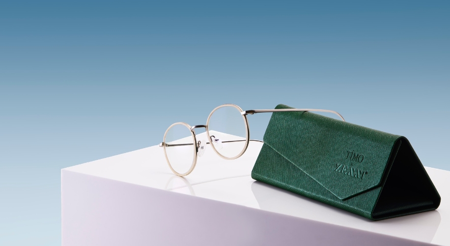 Round eyeglasses with a green triangular case embossed with &quot;TIMO ZANINI&quot; on a white surface.