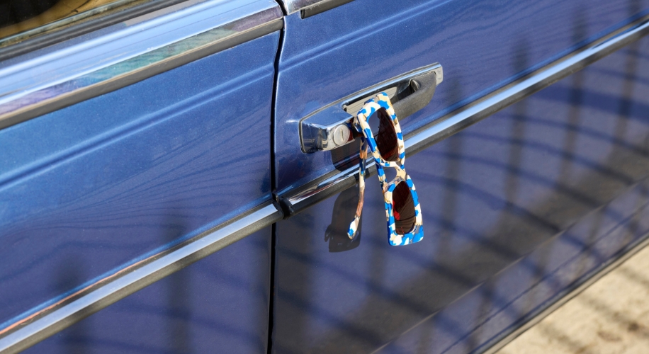 Blue, white, and orange patterned sunglasses hanging on a blue car door handle.