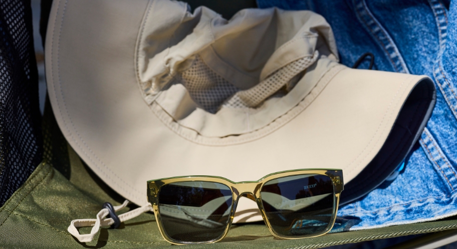 Sunglasses with gold frames and dark lenses set in front of a beige sun hat.