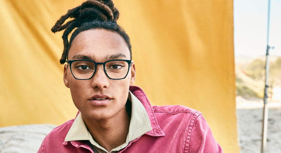 Person wearing black-rimmed eyeglasses and a pink-collared shirt.