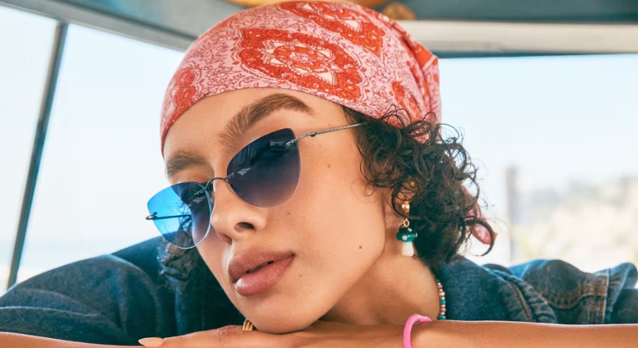 Woman wearing blue-tinted aviator sunglasses, a red patterned bandana, and gemstone earrings.