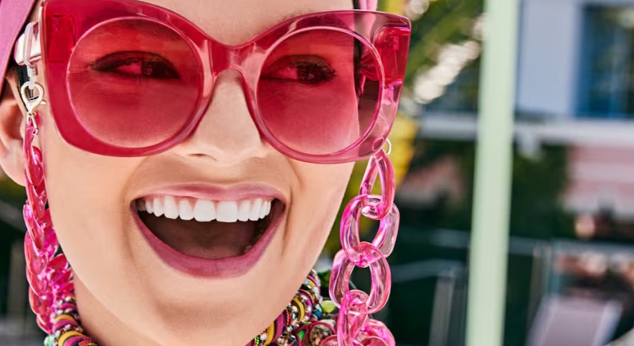 Large pink sunglasses with pink chain and colorful beaded necklace.