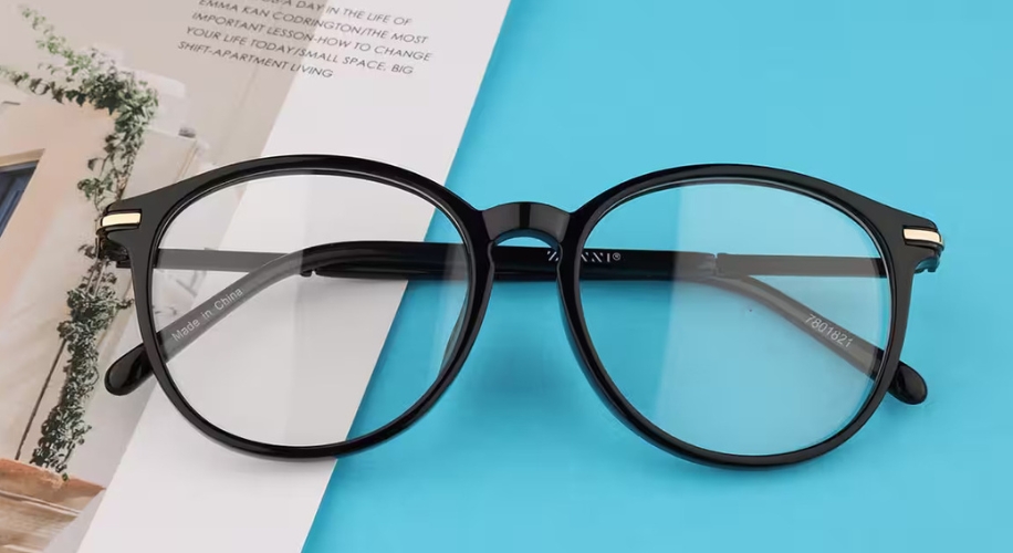 Black round eyeglasses with &quot;Made in China&quot; text on the inner arm, placed on a blue and white surface.